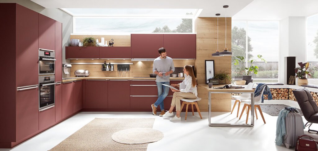 Cocina alemana moderna en Sevilla con muebles en burdeos, distribución en L y zona de comedor abierta al salón, perfecta para espacios contemporáneos.