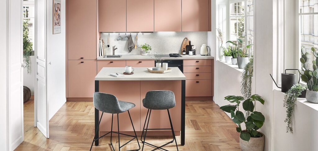 Cocina de diseño pequeño en Sevilla con muebles rosa empolvado, isla funcional y luz natural, ideal para hogares con estilo acogedor y moderno.