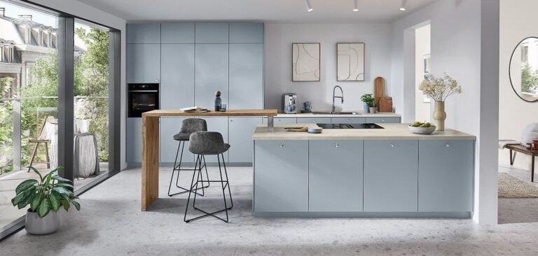 Cocina de diseño actual en Sevilla con isla azul, barra desayunadora de madera y acceso a terraza ajardinada.