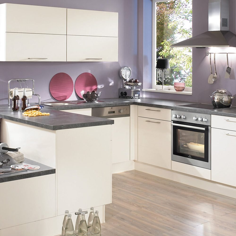 Cocina pequeña en Sevilla con muebles crema, isla con encimera oscura y pared lavanda, ideal para hogares con estilo acogedor y moderno.